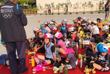 Young athletes in skating gear and helmets sit on a red mat for a speed skating workshop in India.