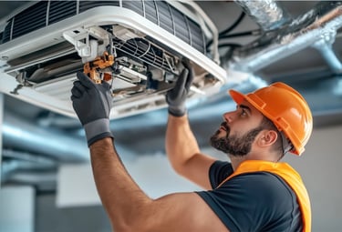 Professional technician in a hard hat performing commercial HVAC repair on a ceiling air conditioning unit.