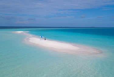 Aerial view of a tropical sandbank in the Maldives with turquoise ocean water and a beach umbrella.