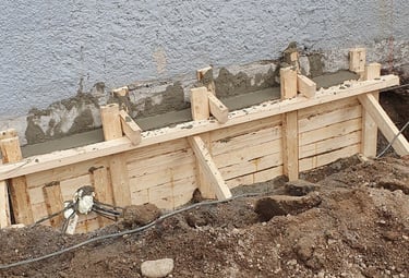 Wooden formwork for a new concrete foundation wall being poured against an existing building.