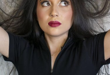 Una mujer con un atrevido lápiz labial rojo y cabello largo y oscuro posa mientras levanta su mechon