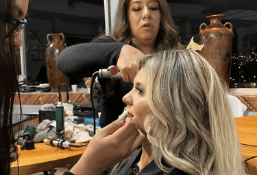 Maquilladora y peluquera profesional preparando a una mujer rubia para un evento especial.