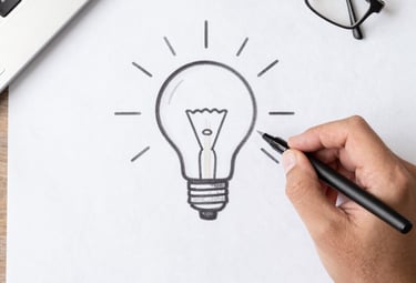 Hand drawing a light bulb idea sketch on paper with a pen at a desk.