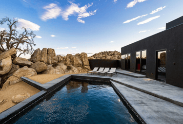 Angular desert-style pool with dark charcoal water and matching dark tiling for a modern, rugged loo
