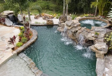 Lagoon pool with dark green water, rock waterfalls and a natural stone interior for a tropical river