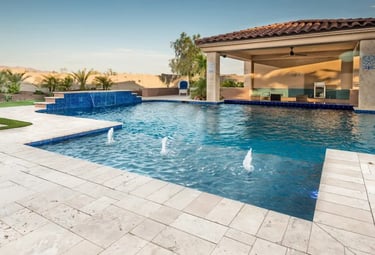 Modern geometric pool with deep blue water and blue mosaic tiles, framed by light stone paving