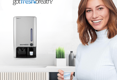 Mujer usando el dispensador de enjuague bucal GotFreshBreath montado en pared, ideal para espacios p