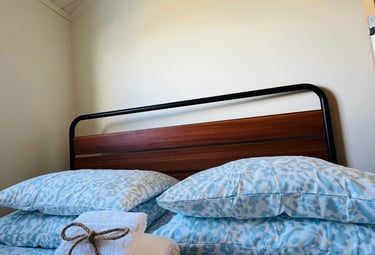 Cozy bedroom interior with blue floral bedding and fresh white towels tied with twine on a wood and metal bed frame.