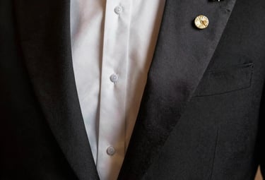 Close-up of a luxurious black tuxedo lapel with silk finish, reflecting soft warm light, showcasing a gold lapel pin, elegant and sophisticated atmosphere, European / Spanish.