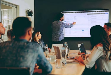 a team watches a colleague point at data on a large screen