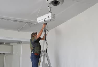 A security camera is mounted on a pole with a large, dome-shaped cover. The structure is composed of metal and plastic with visible screws and mounting hardware. Black cables are connected to the device, and the overall design suggests a robust surveillance setup.