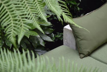 Green outdoor sofa cushions and pillows surrounded by lush garden fern leaves.