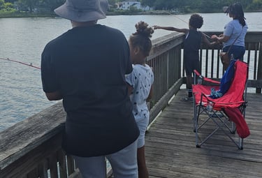 A family fishing together from a wooden pier on a sunny day with blue skies and fluffy clouds.