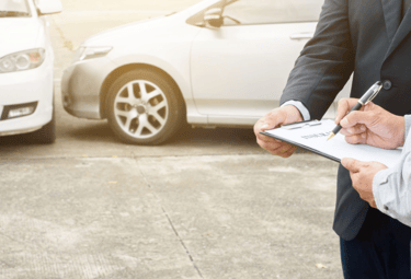 Perito automotriz inspeccionando detenidamente un siniestro de coches, tomando notas
