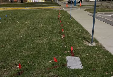 Utility flags and paint marking the location of an underground utility to an inground utility box.