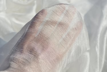 A hand visible through a layer of sheer, white shimmering silk fabric texture.