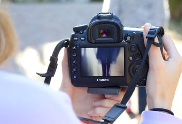 Photographer holding a Canon DSLR camera while reviewing photos on the LCD screen outdoors.