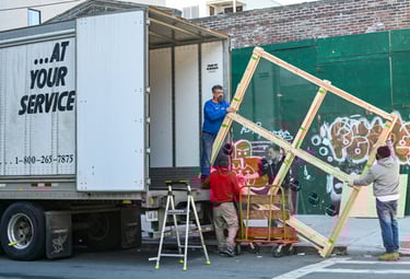 Four people lifting a large window out of a moving truck