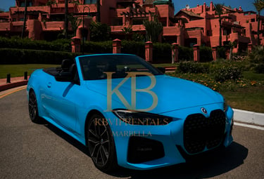Luxury blue BMW convertible rental parked in front of a pink Marbella resort.