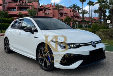 White Volkswagen Golf R parked in front of pink Mediterranean villas in Marbella, Spain.