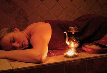 Une femme allongée sur une table de Hammam profitant d'un moment de détente en fermant les yeux.