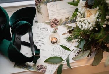 Emerald green velvet wedding heels with rings, floral bouquet, and invitation suite.
