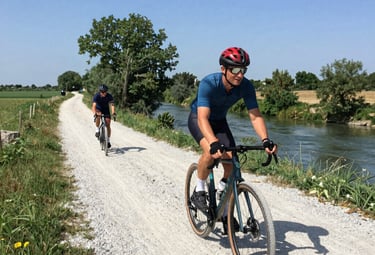 Cyclist on a gravel bike riding along a sunlit country road lined with vineyards.