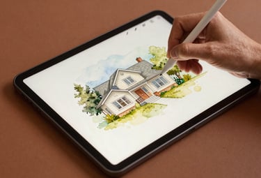 An overhead shot of a North American / US artist using a digital stylus on a tablet to carefully add watercolor textures to a house illustration. The scene is clean and minimal, featuring warm clay brown and cream tones.
