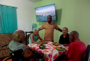 A group of senior citizens enjoying a meal together at a floral-covered table in a community care facility.