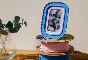 3D printable photo frame on desk with stand and matching colored filament spools
