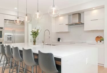 Open-plan kitchen renovation in Sussex featuring a white island with a breakfast bar, lighting, and integrated appliances.
