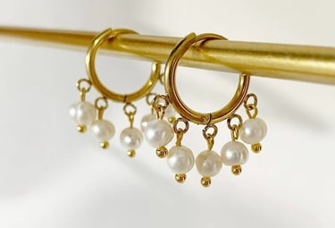 Elegantes aros dorados con dijes de perlas blancas colgantes en una barra de exhibición dorada.