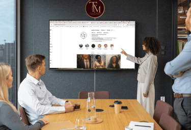 a group of people sitting around a table with a man pointing at a screen