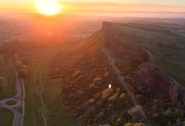 Aerial view of Salisbury Crags in Edinburgh at sunset with the city skyline in the background.