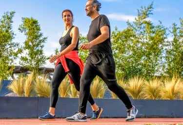 Casal caminhando ao ar livre em pista cercada por plantas, em dia ensolarado.