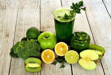 Copo de suco verde sobre mesa de madeira, acompanhado de maçã verde, limão, kiwi, pimentão, brócolis