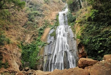 A scenic multi-tier tropical waterfall cascading down a steep rocky cliff surrounded by lush green vegetation.