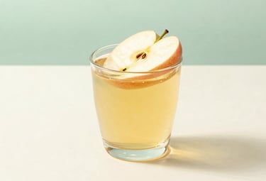 A minimalist studio shot of a glass of golden apple juice with a single thin slice of fresh apple floating on top. The glass is placed on a smooth, creamy white surface. The lighting is soft and professional, creating a sophisticated and clean aesthetic. Palette includes soft mint green and creamy white.