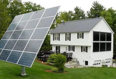 Ground-mounted solar panel array tracking the sun next to a residential home with solar thermal collectors.
