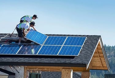 Professional solar installers mounting blue photovoltaic panels on a residential asphalt shingle roof.