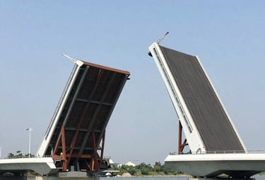 A futuristic movable bridge lifting to allow ships to pass under a bright blue sky.