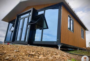 Modern prefabricated modular cabin with wood siding and large glass windows on a rocky foundation.