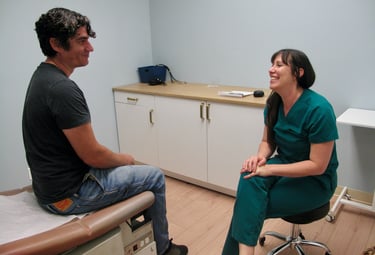 A smiling doctor in green scrubs consulting with a male patient in a medical exam room.