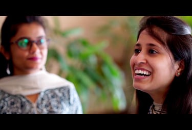 a woman with glasses and a scarf looking at another woman who is smiling