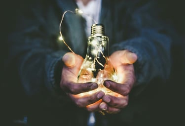 an older man holds a lightbulb, symbolizing the knowledge and mentorship he is providing