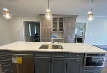 Remodeled kitchen island in dark gray with white veined quartz and light gray cabinets.