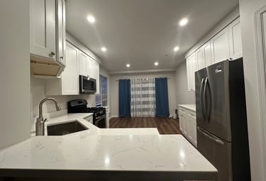 Renovated kitchen with white shaker cabinets, quartz counters, and a stainless steel fridge.