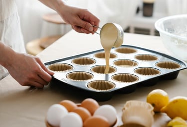 Panadero vertiendo masa para cupcakes en un molde para muffins con capacillos.