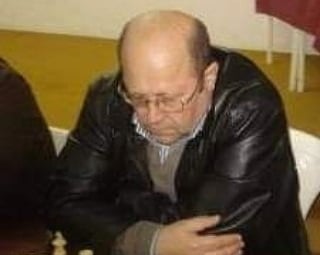 A focused male chess player wearing glasses and a leather jacket during a competitive chess tournament match.