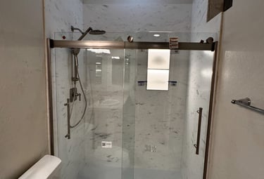 Modern bathroom remodel featuring a walk-in shower with sliding glass doors and marble wall panels.